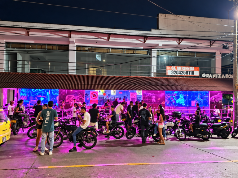 Fachada nocturna de Max Cocktail Barranquilla Sur La 8, con iluminación neón y clientes frente al local.