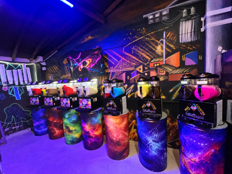 Interior de Max Cocktail Buenos Aires en Medellín, con máquinas de granizados, bases cósmicas y mural del barrio.