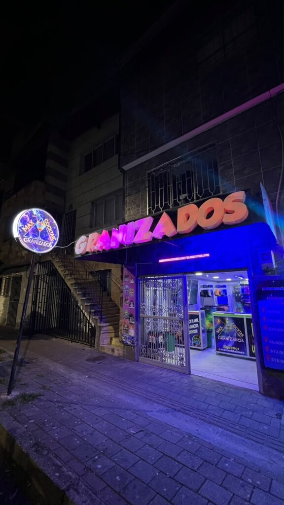 Fachada nocturna de Max Cocktail El Salvador con aviso de Granizados y luces neón.