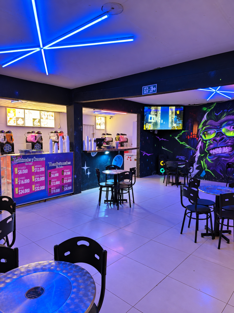 Interior de Max Cocktail La Jagua de Ibirico con mesas, máquinas de granizados y mural de colores neón.